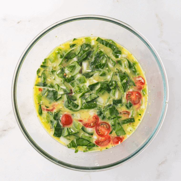 Folding in cherry tomatoes, spinach, diced onion, and chopped bell peppers.