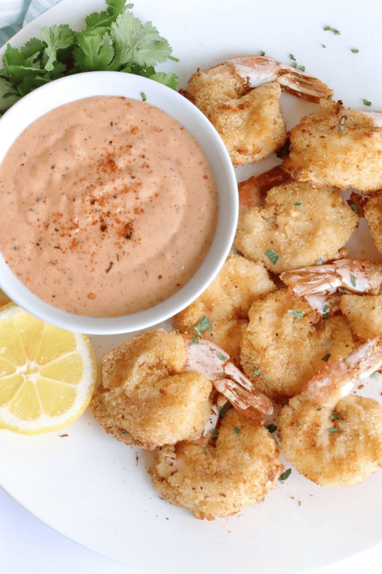 Plate of homemade Long John Silver's battered shrimp served with tartar sauce, lemon wedges, and crinkle-cut fries on a white counter