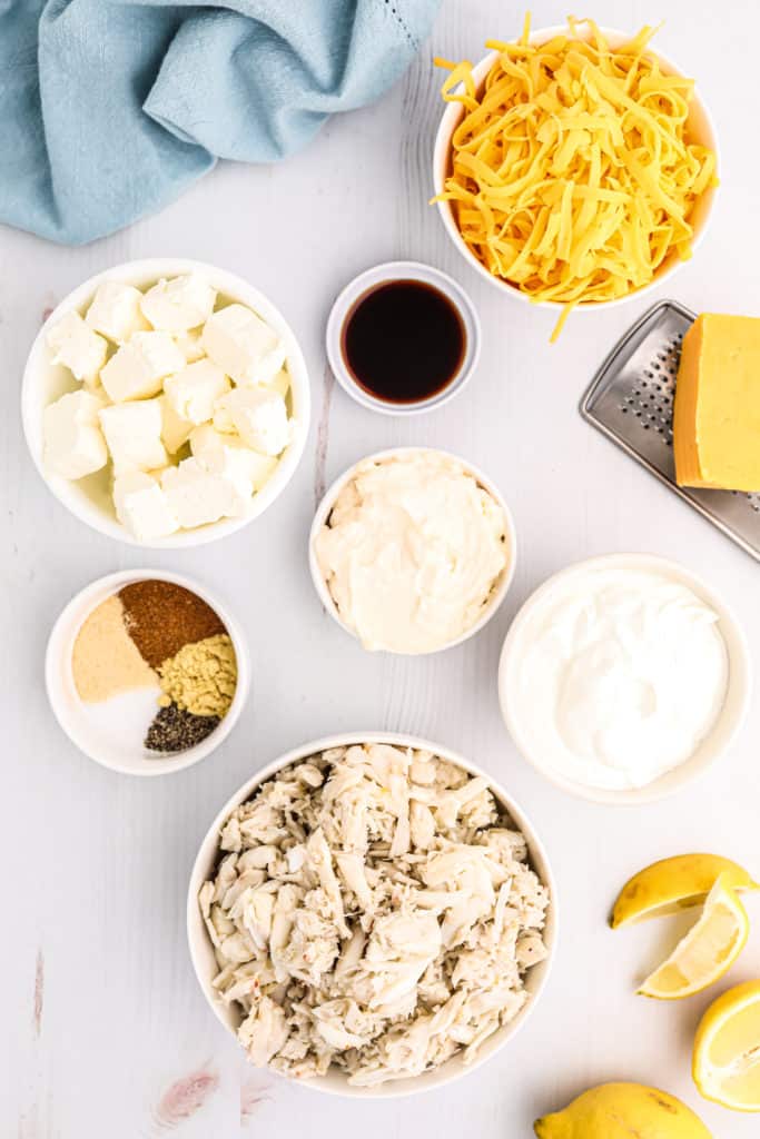 Ingredients for Air Fryer Hot Crab Dip, including crab meat, cream cheese, garlic, herbs, and spices, arranged on a wooden cutting board.