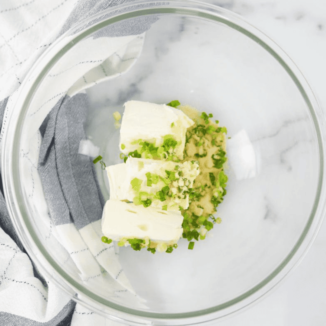 Placing a wonton wrapper on a flat surface and adding a generous mixture of cream cheese, minced scallions, and spices.