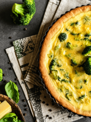 Slice of air fryer broccoli cheddar quiche on a white plate with a golden, flaky crust