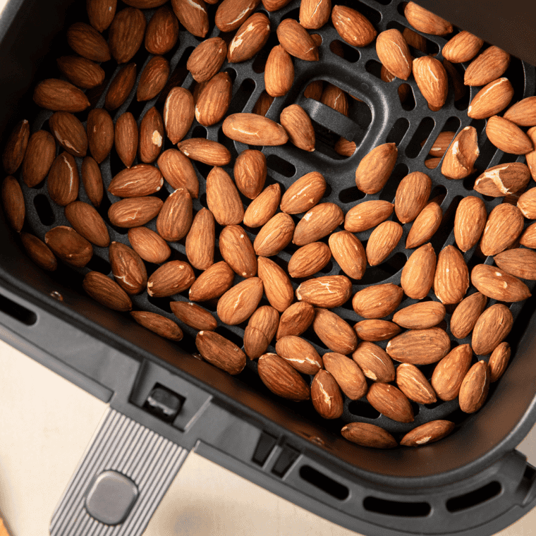 Coated almonds spread in a single layer in the air fryer basket before cooking