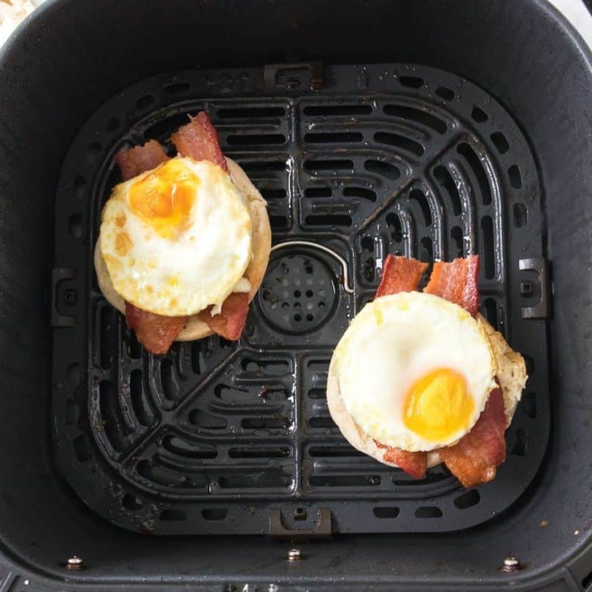Assembling an Egg McMuffin in the air fryer with English muffin, sausage, egg, and cheese before melting.