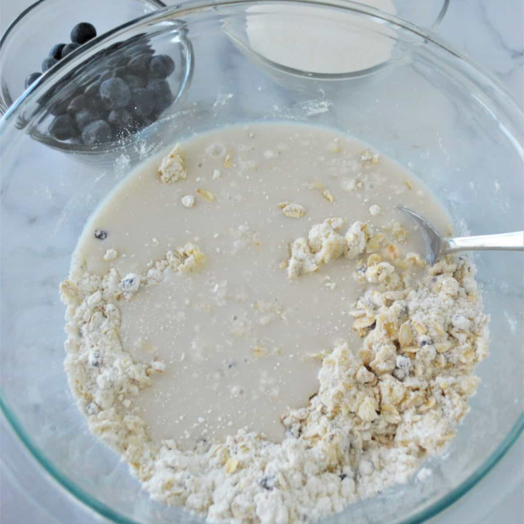 Mixing blueberry muffin batter with banana, oats, and fresh blueberries in bowl