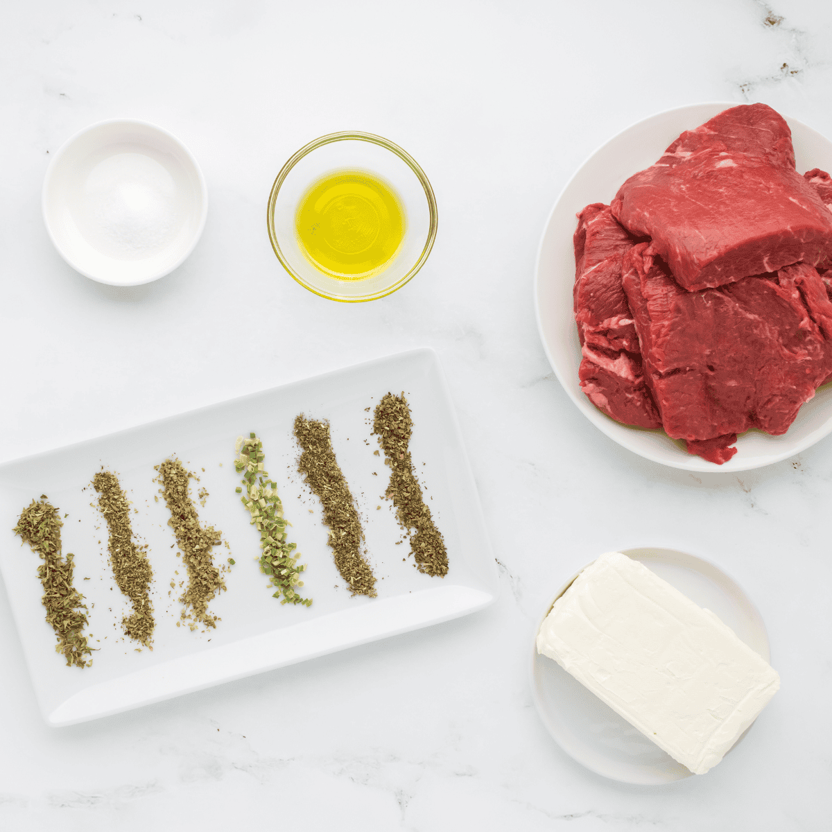 Flat iron steaks, olive oil, kosher salt, and black pepper laid out on a marble counter.