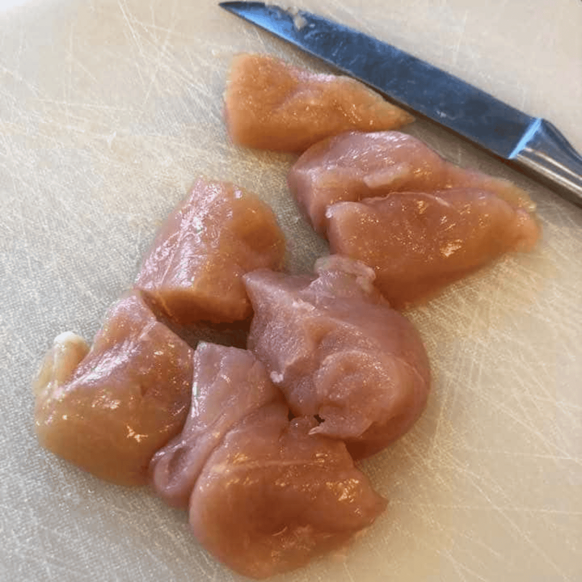 Raw chicken breast diced into 1-inch pieces on a cutting board.
