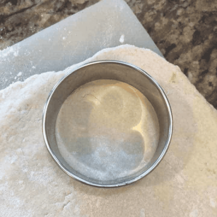 Bisquick dough being mixed in a bowl, rolled out, and cut into biscuit shapes with a cutter.