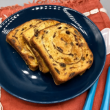Golden air fryer cinnamon raisin french toast stacked on a white plate with maple syrup and powdered sugar