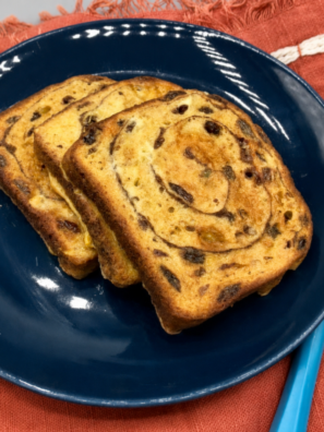 Golden air fryer cinnamon raisin french toast stacked on a white plate with maple syrup and powdered sugar