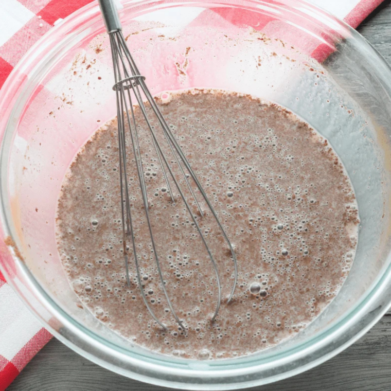 Whisking eggs, milk, flour, vanilla, and cinnamon into a smooth french toast custard in a pie plate