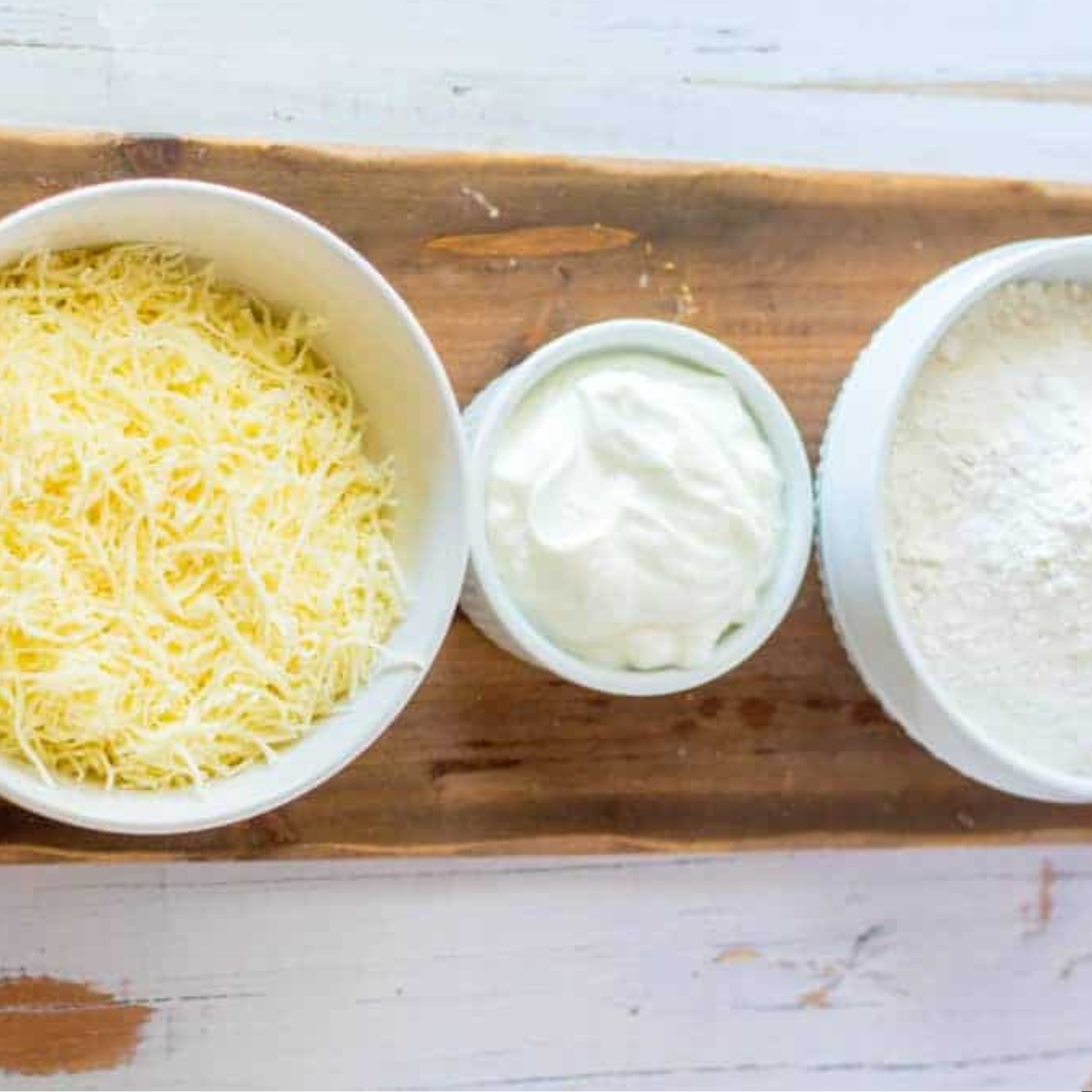 Ingredients for Air Fryer Asiago Cheese Bagels, including flour, baking powder, Greek yogurt, and shredded Asiago cheese, arranged on a kitchen counter.