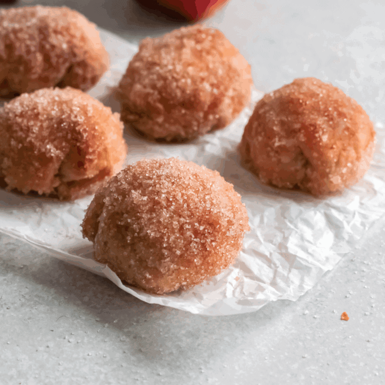 Golden homemade Dunkin' Donut Munchkins coated in powdered and cinnamon sugar, served on a plate.
