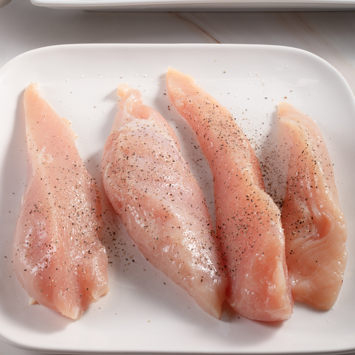 Chicken thighs being seasoned with a spice blend in a small bowl before being wrapped in bacon for air frying