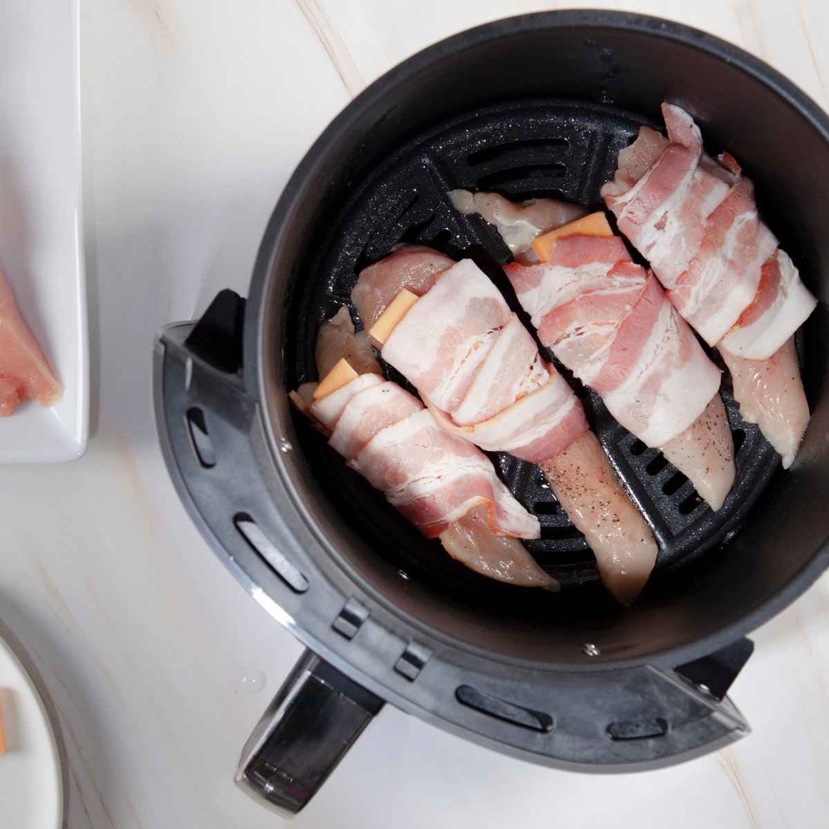  Chicken wrapped in bacon being flipped inside an air fryer basket using tongs