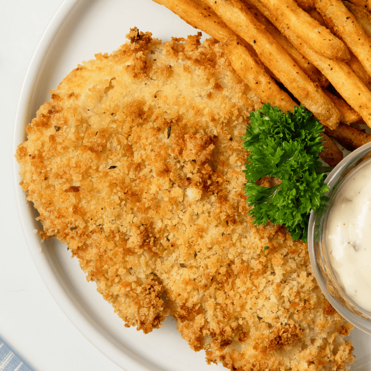 Golden, crispy air fryer frozen haddock served on a plate with lemon wedges and garnish.