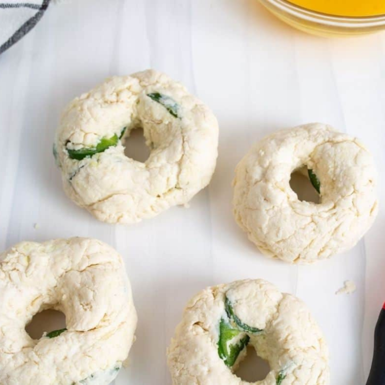 Four jalapeño cheddar bagels shaped into rings on a floured surface, ready for the air fryer
