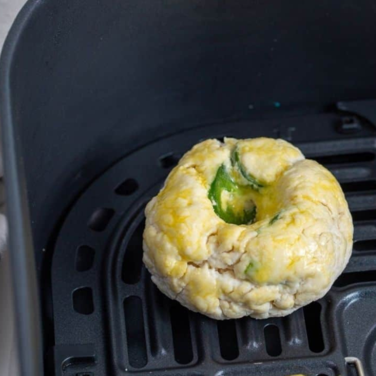 Jalapeño cheddar bagels arranged in a single layer inside an air fryer basket before cooking