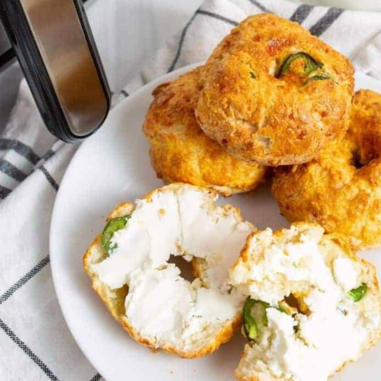 Golden air fryer jalapeño and cheddar bagels topped with melted sharp cheddar and fresh jalapeño slices on a wooden board