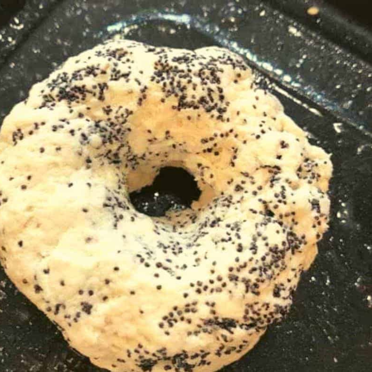 Shaping Poppy Bagels: A hand shaping the dough into bagel forms on a countertop.