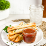 Golden brown Air Fryer Wonton Mozzarella Sticks stacked on a plate with melted cheese and a side of marinara sauce.