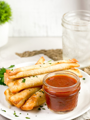 Golden brown Air Fryer Wonton Mozzarella Sticks stacked on a plate with melted cheese and a side of marinara sauce.