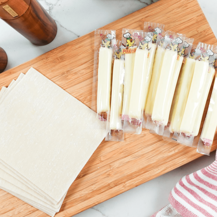 Unwrapping a mozzarella cheese stick and placing it at the end of an egg roll wrapper.