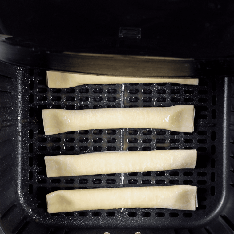 Spraying wrapped mozzarella sticks with olive oil spray before air frying at 350°F for 5–9 minutes."