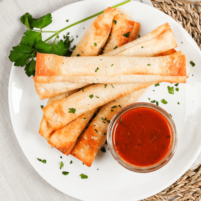 Golden brown Air Fryer Wonton Mozzarella Sticks with gooey cheese inside, served with a side of marinara sauce.