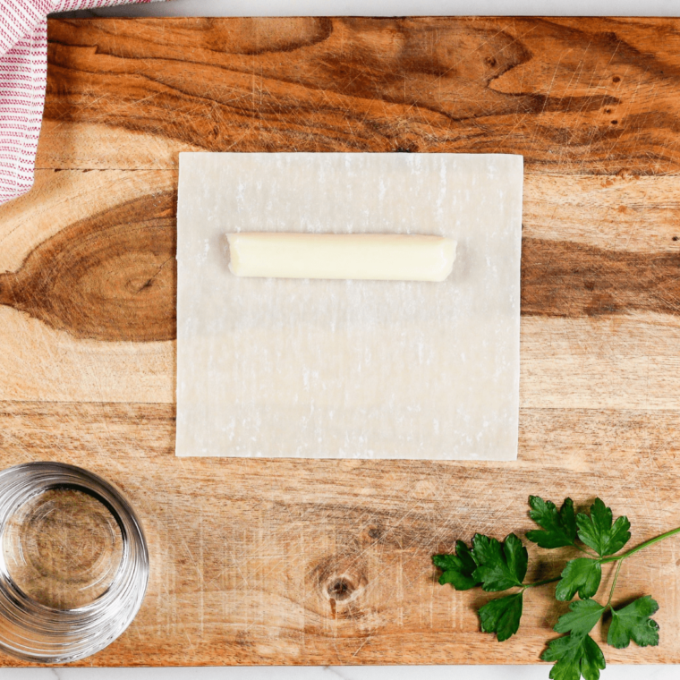 Leaving an inch at the end of the egg roll wrapper, wetting edges with water, and pinching the wrapper to seal the mozzarella stick inside.