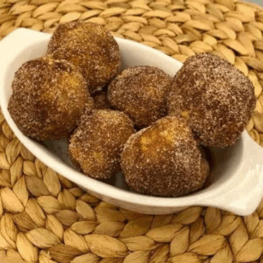 Golden air fryer biscuit donut holes coated in cinnamon sugar and served on a plate.