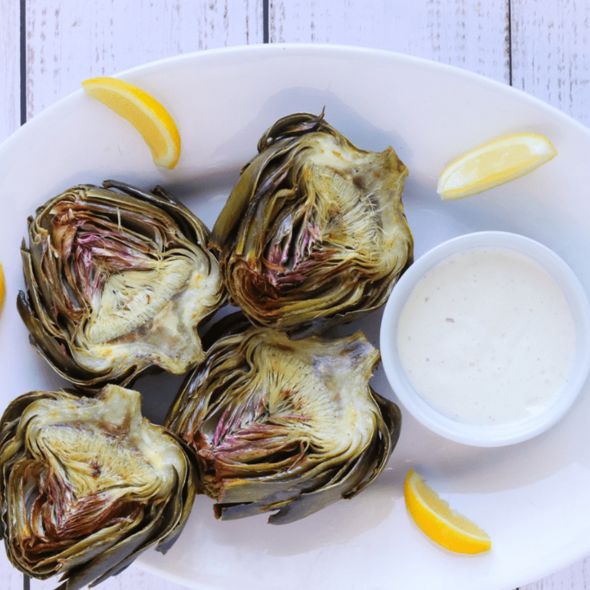 Crispy air fryer artichokes cut side up on a plate with garlic aioli and lemon wedges