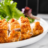 Air fryer chicken costoletta on a white plate, drizzled with lemon cream sauce and topped with chopped parsley