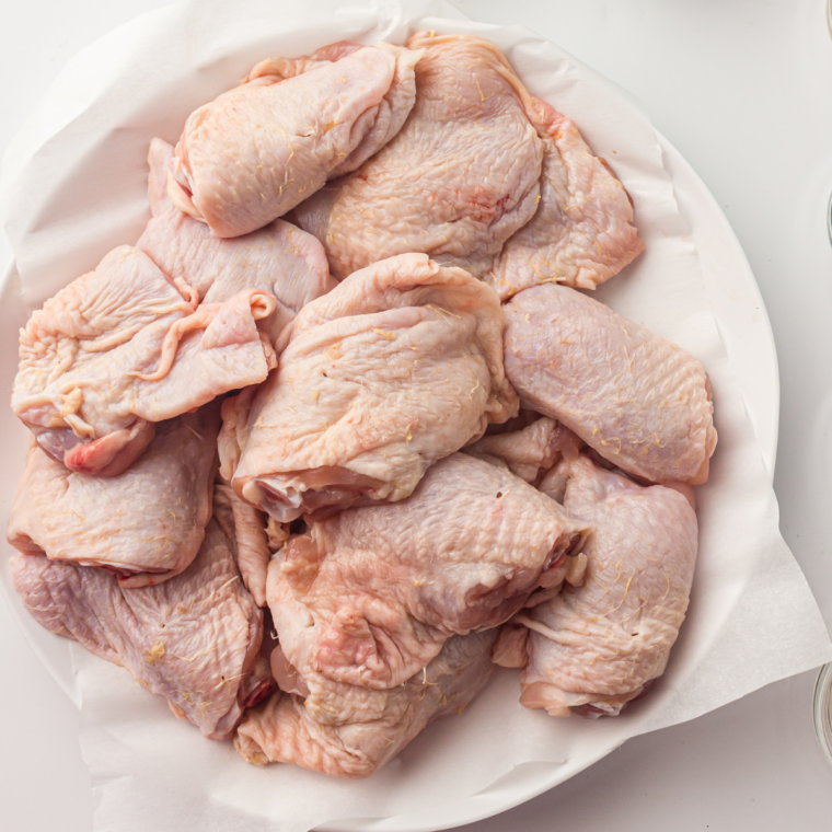 Raw chicken thighs being patted dry with a paper towel on a cutting board