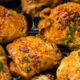 Air fryer pesto chicken thighs in a black air fryer basket, coated in green basil pesto with browned crisp edges