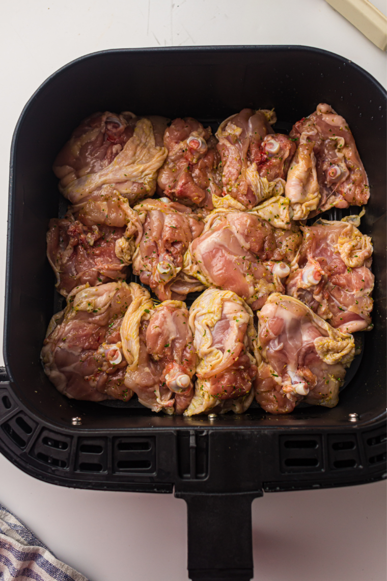 Chicken thighs being turned in pesto marinade with tongs until fully coated
