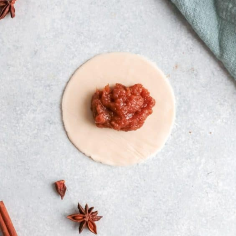 Filling pie dough circles with pumpkin mixture, folding them into half-moon shapes, and pressing the edges to seal before air frying.