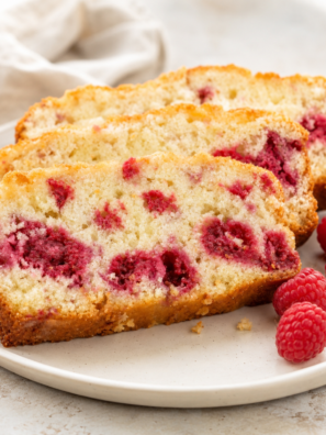 Sliced air fryer raspberry bread on a wooden board with fresh raspberries visible throughout the crumb