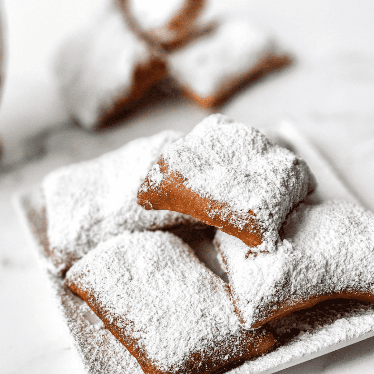 Golden, fluffy Copycat Cracker Barrel Beignets dusted with powdered sugar on a serving plate.