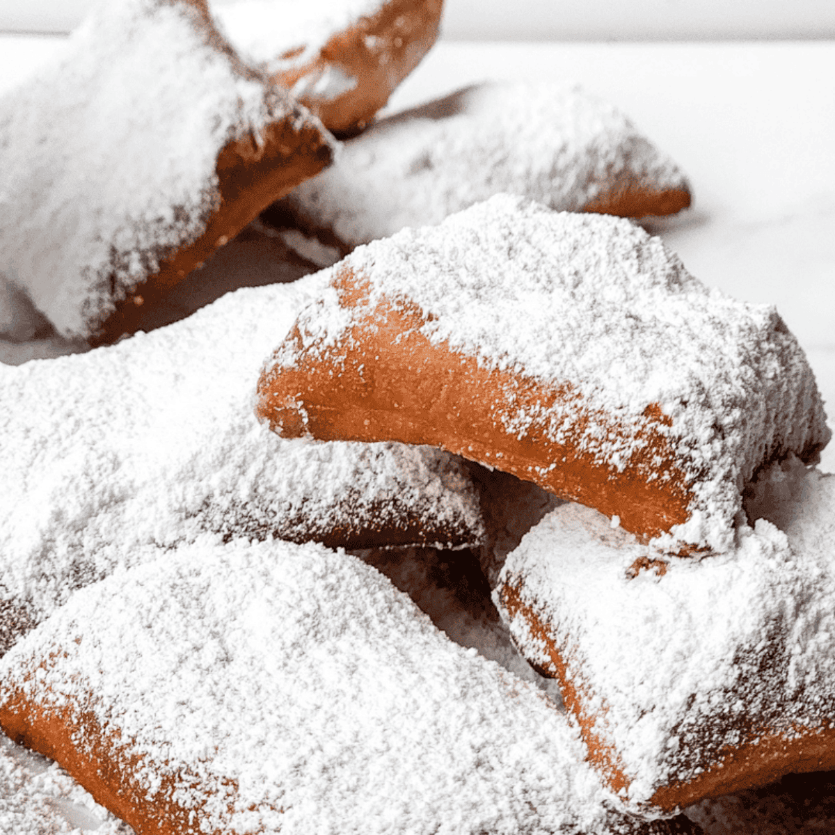 Golden, puffy beignets dusted with sugar on a white plate.