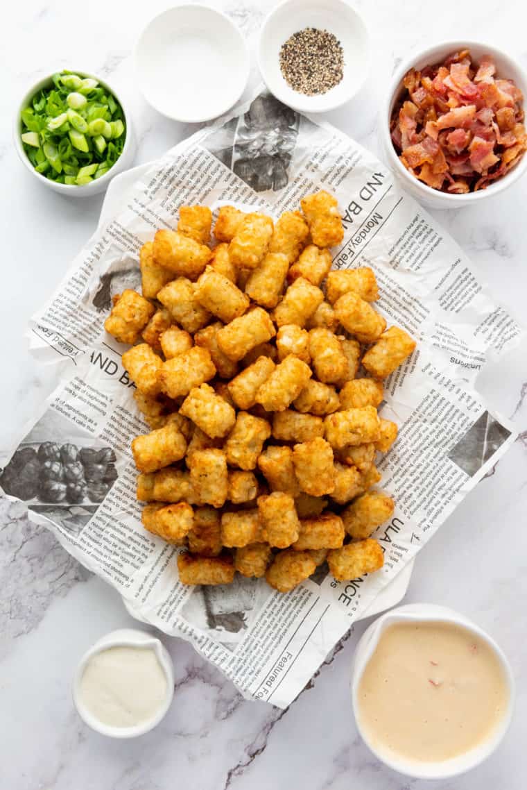Overhead view of crispy loaded tater tots cooked in the air fryer, surrounded by small bowls of toppings like cheese, bacon, and green onions.