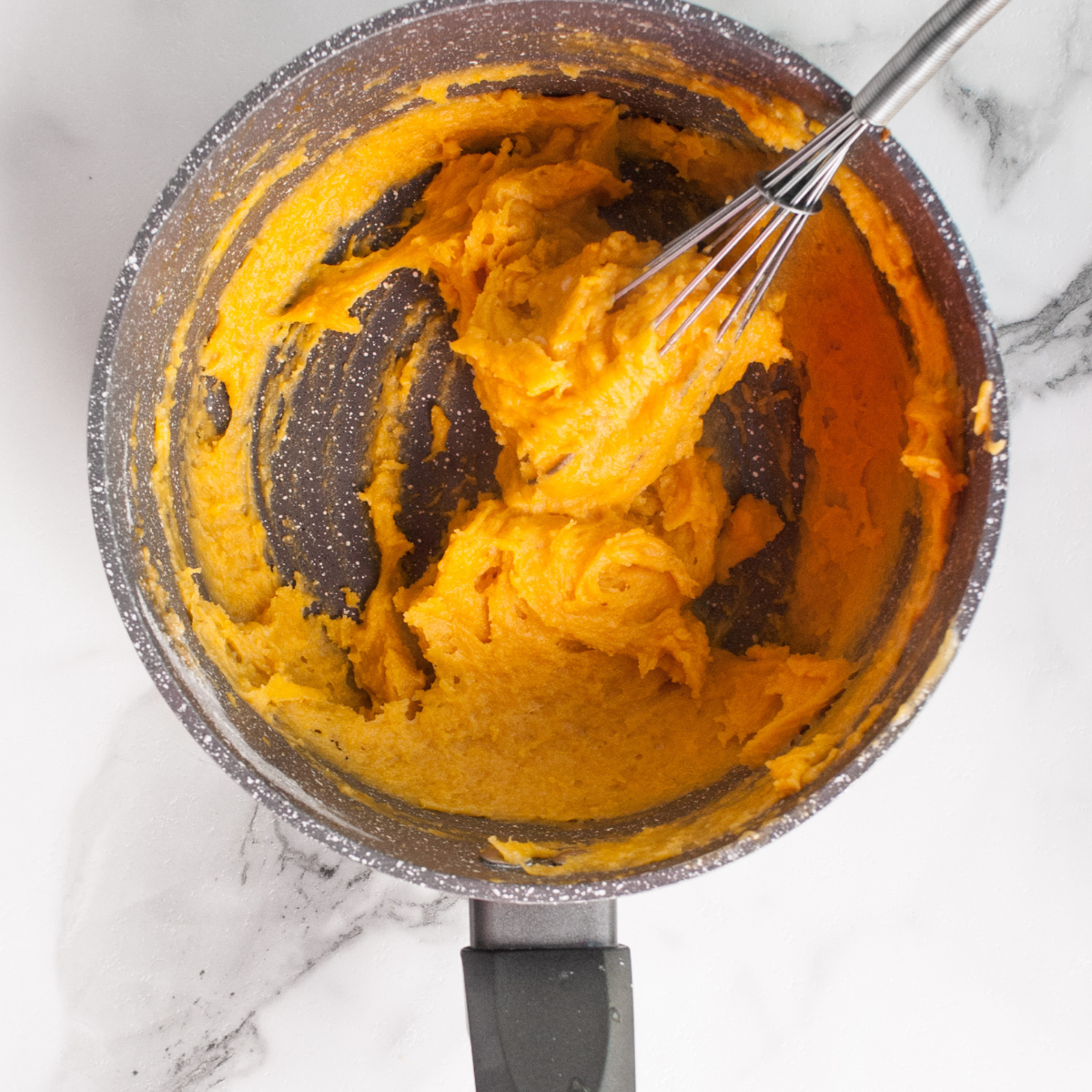 Mixing bowl with wet pumpkin ingredients being combined with dry flour mixture to make smooth donut batter.