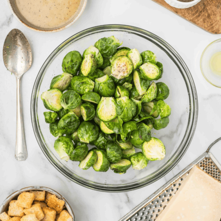 Brussels sprouts in a bowl tossed with oil, butter, sugar, salt, and pepper.
