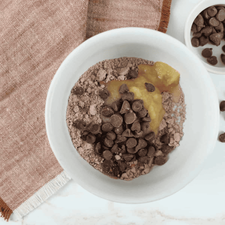 A small bowl filled with cake mix, water, unsweetened applesauce, and chocolate chips being mixed together.