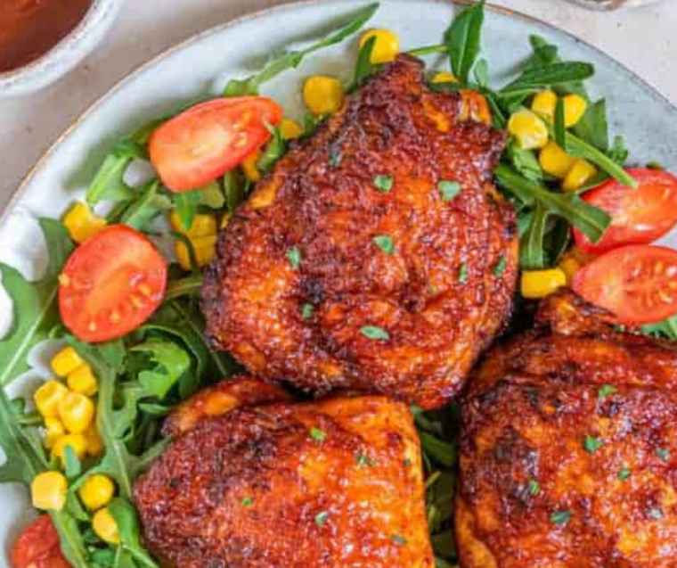 Air fryer BBQ chicken thighs served on a plate with coleslaw and corn on the cob