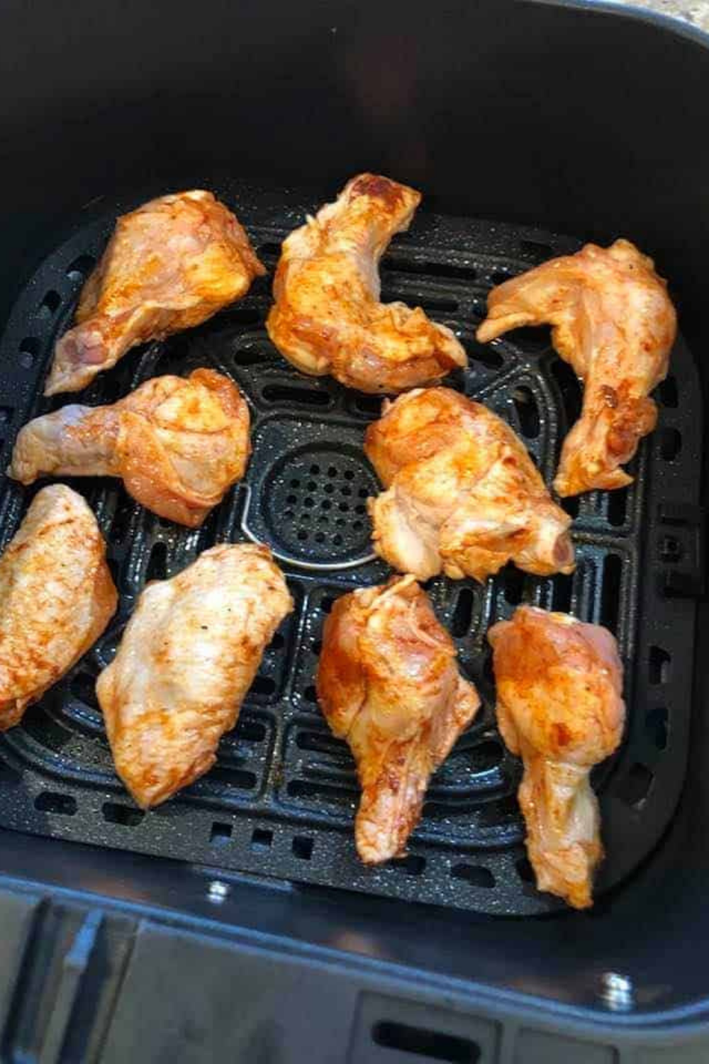Placing seasoned chicken wings in the air fryer basket in a single layer