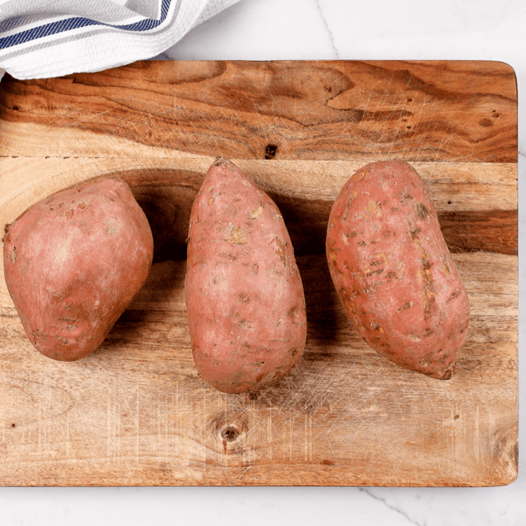 Whole raw sweet potatoes on a wooden cutting board