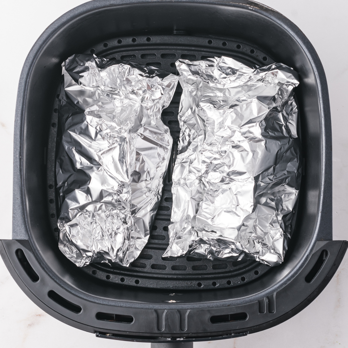 Zucchini foil packets being placed into the air fryer basket.