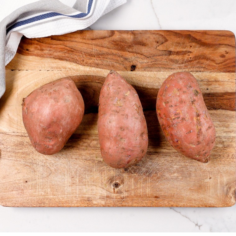Chopping peeled sweet potatoes into 1- to 2-inch pieces on a cutting board.