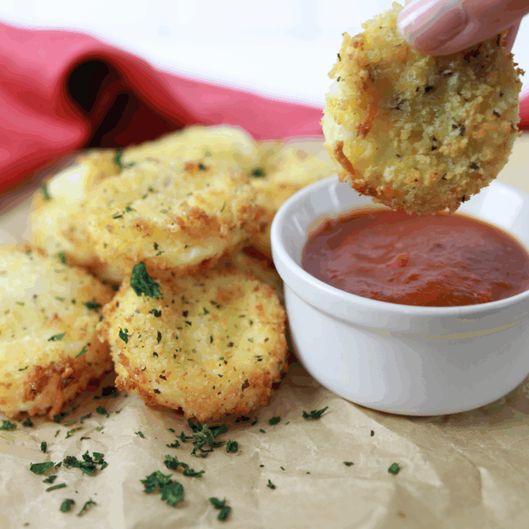 Hand dipping a crispy air fryer Babybel cheese bite into a small bowl of marinara sauce
