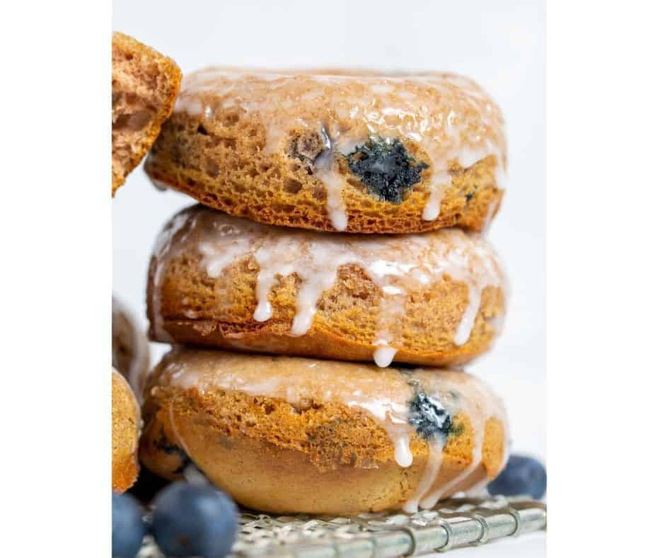 A close-up of blueberry donuts with a glossy glaze and scattered fresh blueberries around them on a white background.